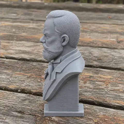 3D-printed bust of a bearded man in a suit, viewed in profile on a wooden surface.