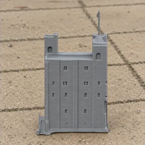 A 3D-printed gray model of a castle tower with small windows and a flag on top.