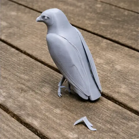 Gray 3D-printed model of a bird, possibly a hawk, with a detached claw on wood surface.
