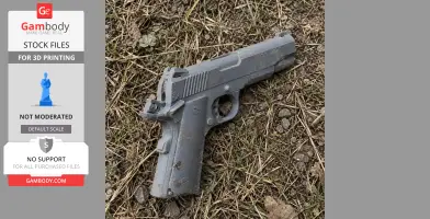 A 3D-printed gray Colt Officer's ACP prop pistol lying on grass and dirt.