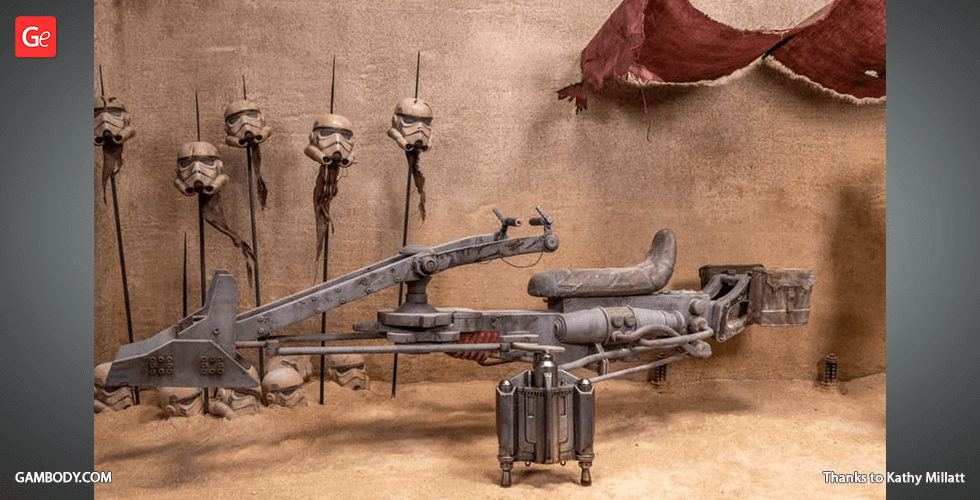 A detailed Mandalorian speeder bike model in a desert setting with helmets on spikes in the background.