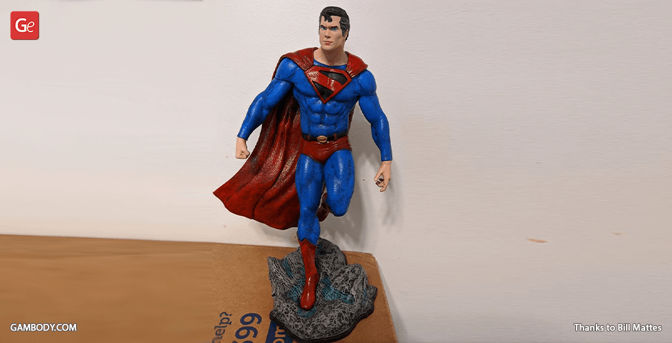 A classic Superman 3D printed model in a blue suit and red cape, standing heroically on a stone base.