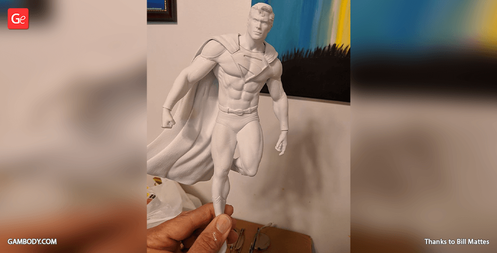 3D-printed model of a muscular superhero in a cape, posed mid-flight, held in someone's hand.